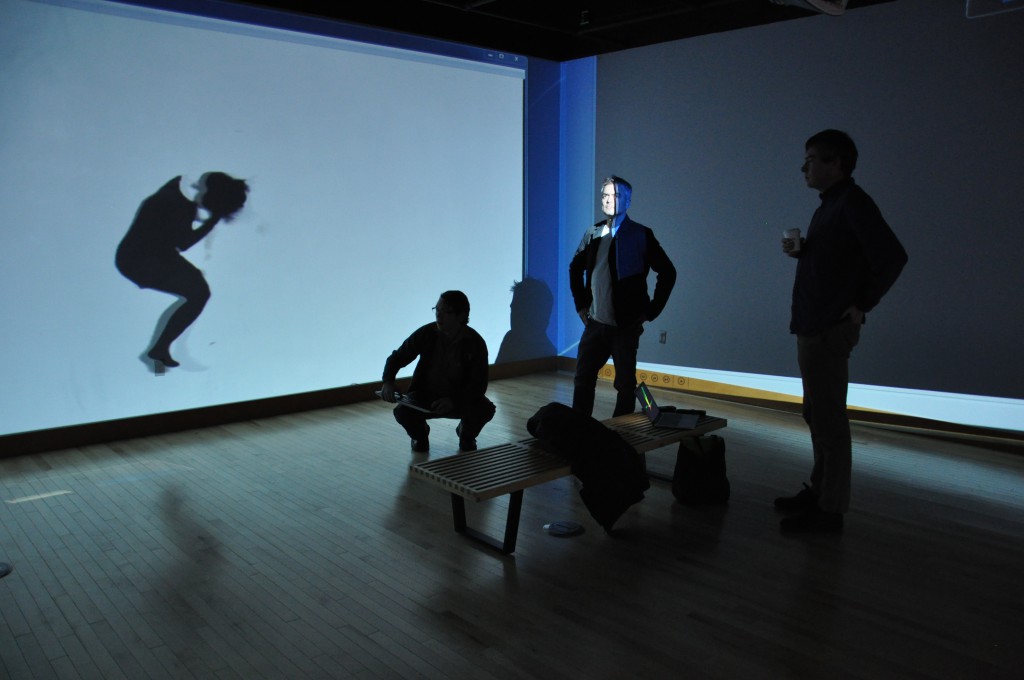 Cris Moss, center, prepares with UO staff Chris Cosler (left) and artist Carl Diel (right) to set up a video installation in the Gray Box.  Projected on the wall is "Wrest_01," work by artist Heidi Schwegler exhibiting in the Gray Box.