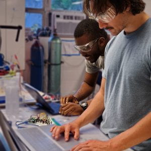 two students working with electrochemical equipment and a computer in a laboratory