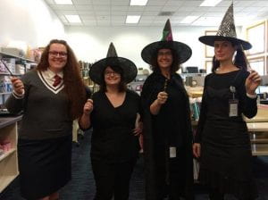 Four women dressed as witches. Three are wearing black and have pointy hats, the fourth is dressed like a Hogwarts student from the Harry Potter series. They all have wands.