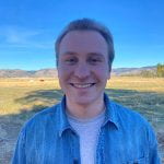 Photo of the author smiling while wearing a denim shirt in front of a sunny Eastern Oregon landscape
