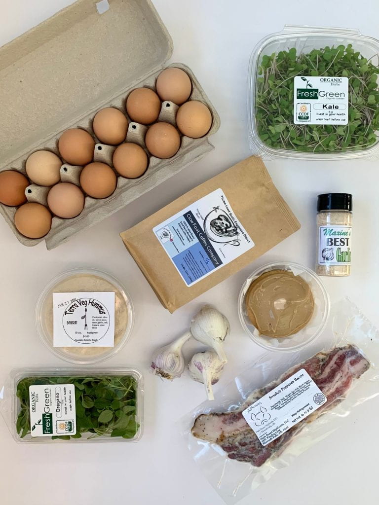 A selection of food available through the Klamath Falls Online Marketplace: eggs, kale, coffee, hummus, garlic, garlic salt, oregano, and bacon. 