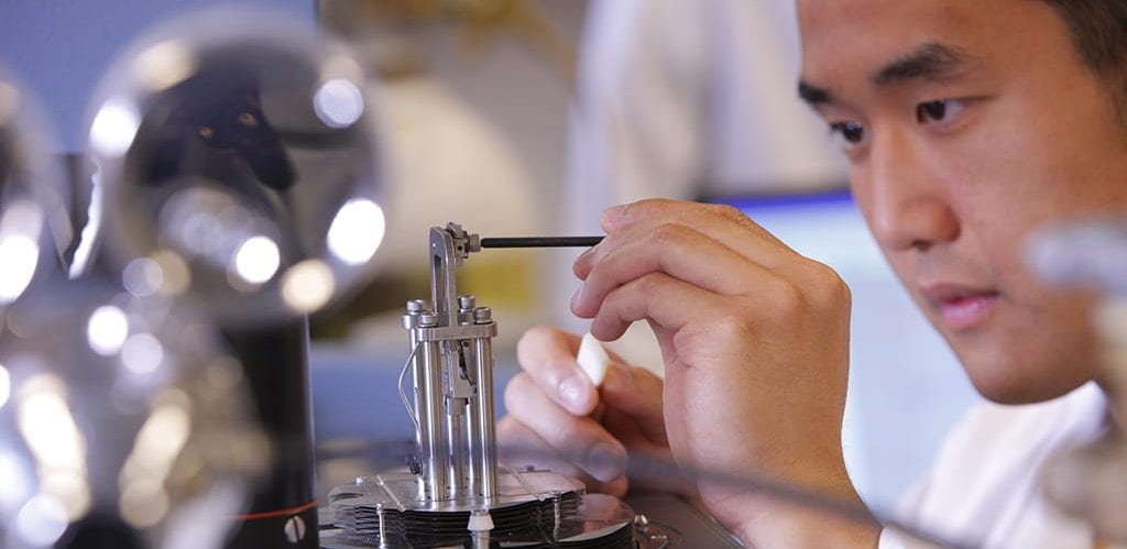 A male college student working with equipment in a science lab, focused on the task at hand.