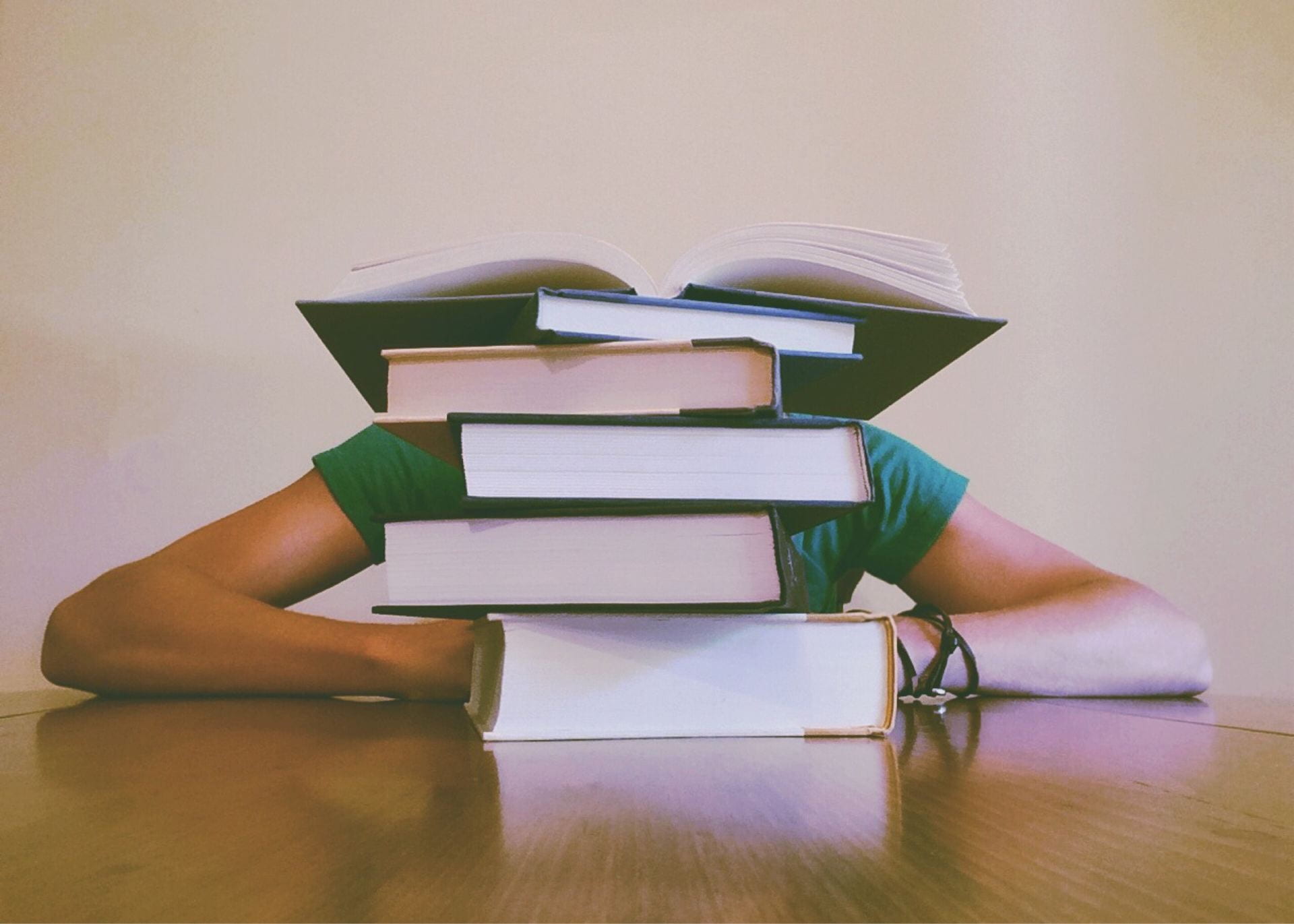 An image of a student at a table with books stacked blocking their face.