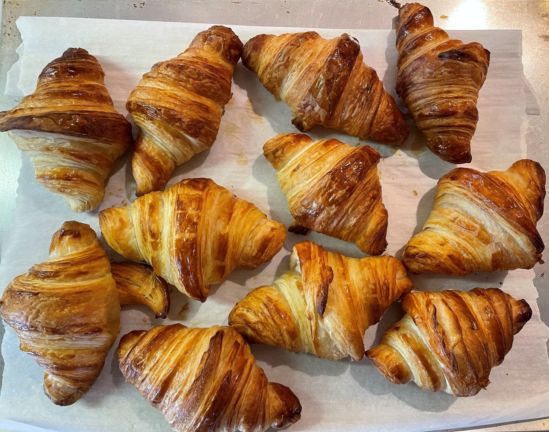 11 golden-brown freshly-baked croissants on parchment paper