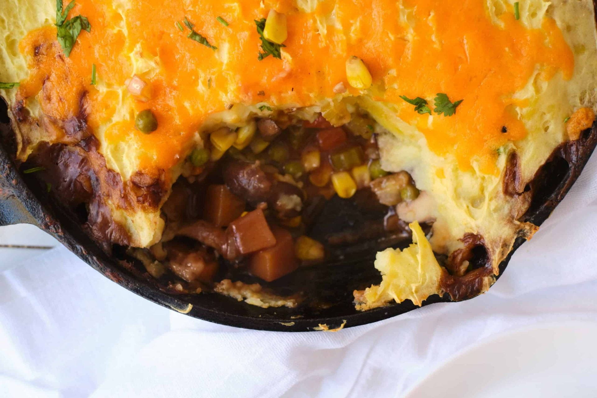 Cast iron pot containing vegetarian shepherd's pie; potato and cheese topping, carrots, beans and corn visible in spooned out section