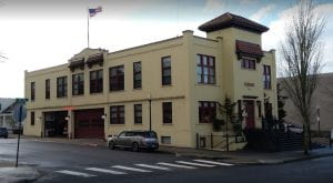 Beige two-story building with red fire engine and garage doors visible; red-framed windows; US flag flying