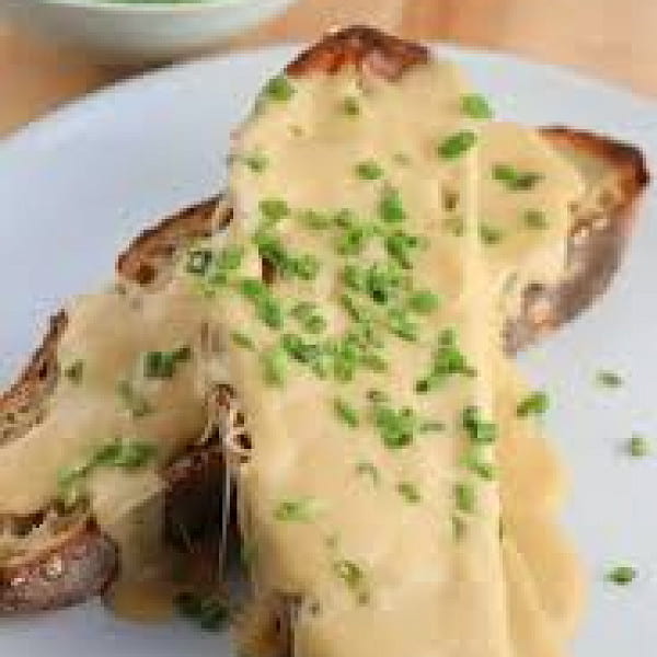 Cheese sauce on toast with herbs on top; two slices arranged on a white plate
