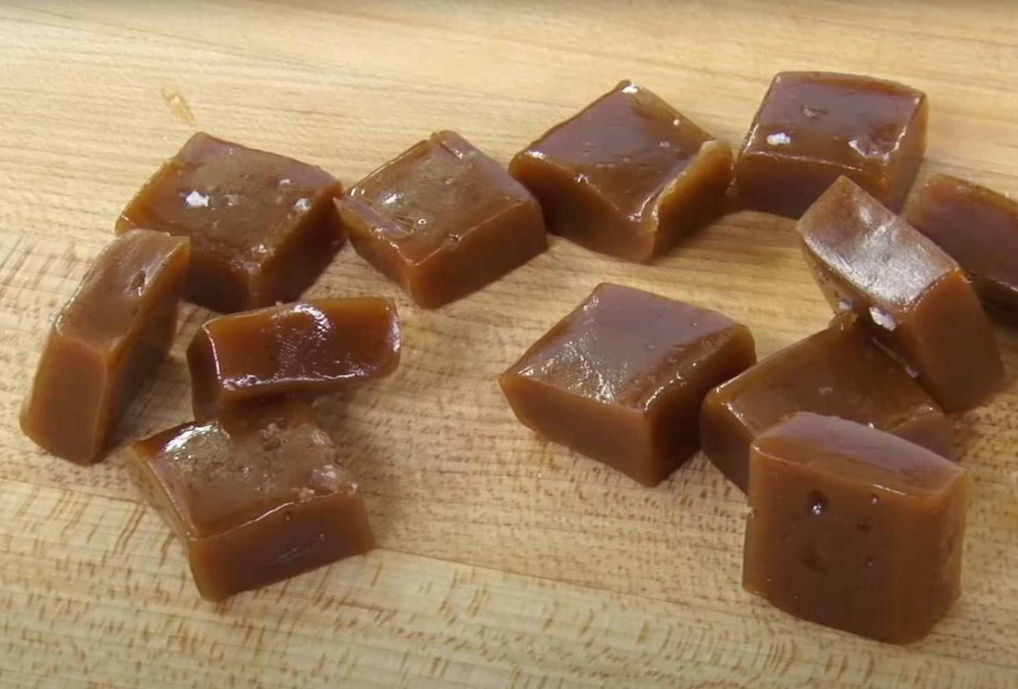 12 dark brown soft caramel squares with flecks of white salt occasionally visible; on a brown wooden counter top
