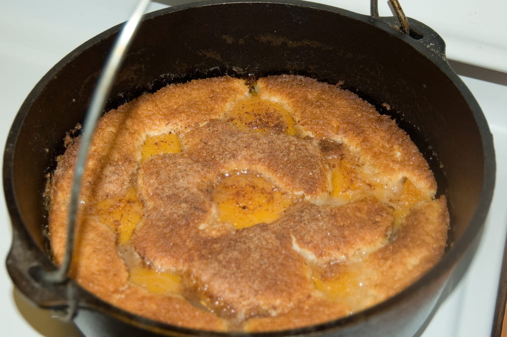 Cast iron Dutch Oven with the handle up; visible in the bottom of the cast iron pot is a cinnamon-sugar-peaches-cake mixture