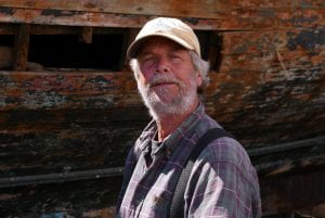 Knute Nemeth an old white man with a grey beard, purple plaid shirt, and tan baseball cap.