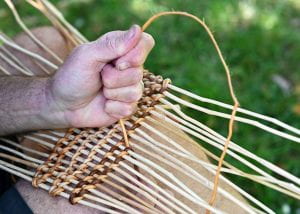 White hands of a man weaving straw into a basket
