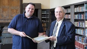 Two people hold an opened folder containing blue papers. 