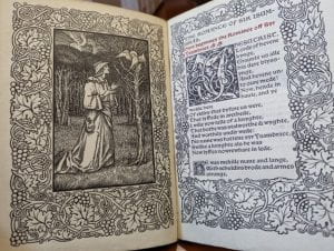 Two pages from an elaborately illustrated book, with a grapevine border. A robed figure kneels in front of a bare tree, in which a haloed dove rests. 