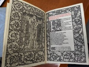 Two open pages of an elaborately illustrated book. Floral and leaf-like patterns border a doorway in which two people embrace. 