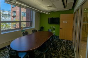 An image of a small meeting room with a round table, chairs and a wall-mounted TV.