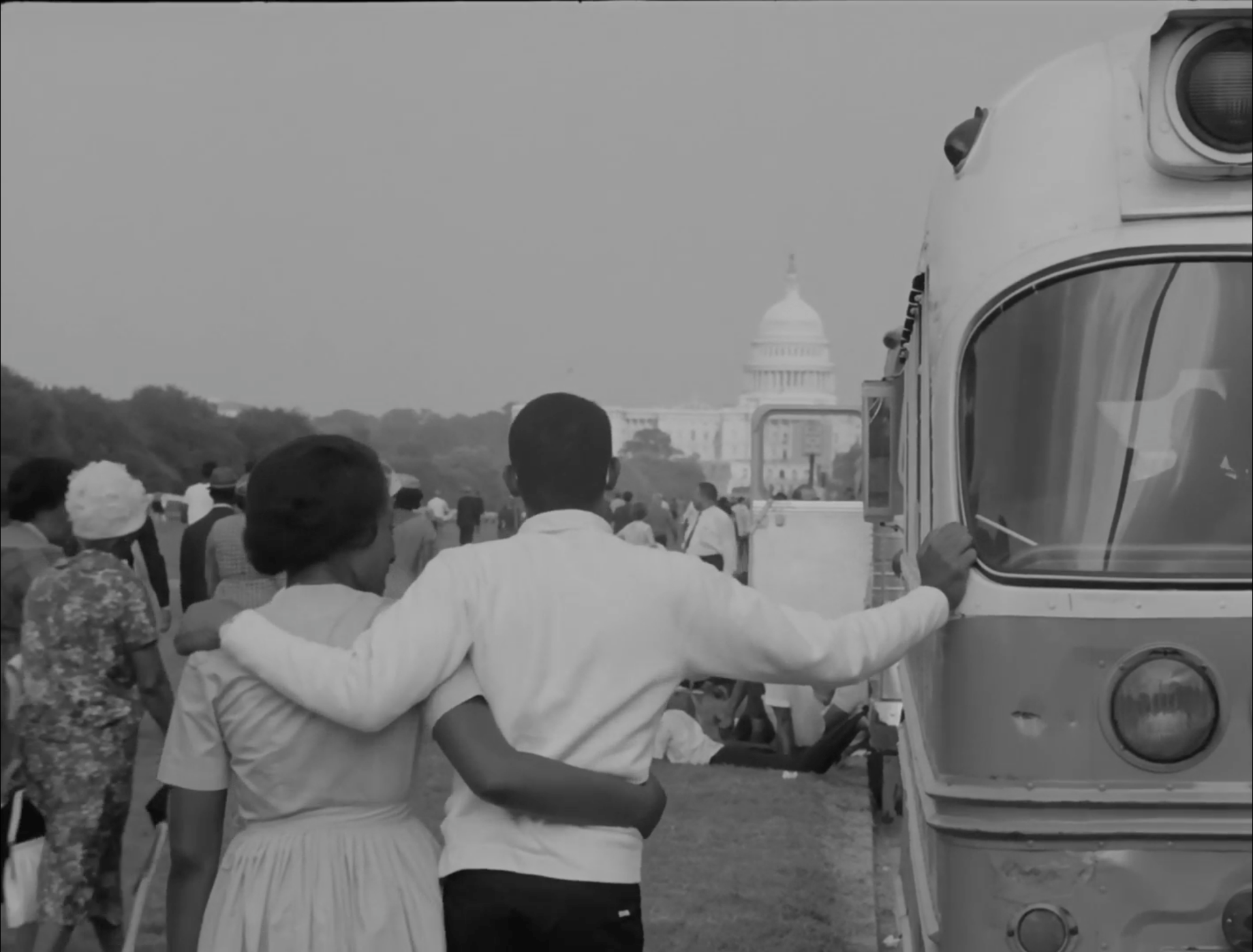 Two people stand arm in arm in front of the US Capitol building.