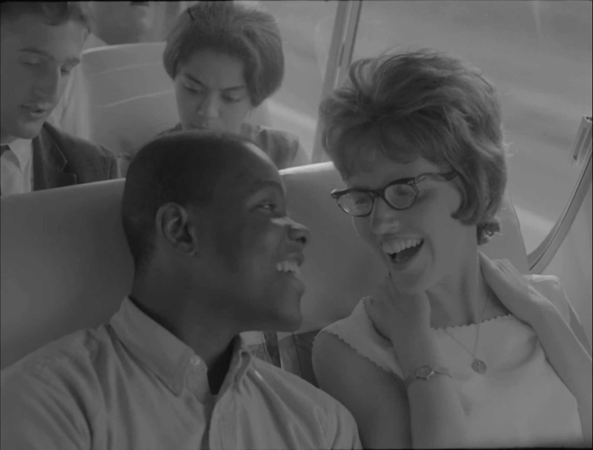 A man and a woman laugh while sitting next to each other on a bus.