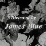 A film still showing people singing with the title "Directed by James Blue."