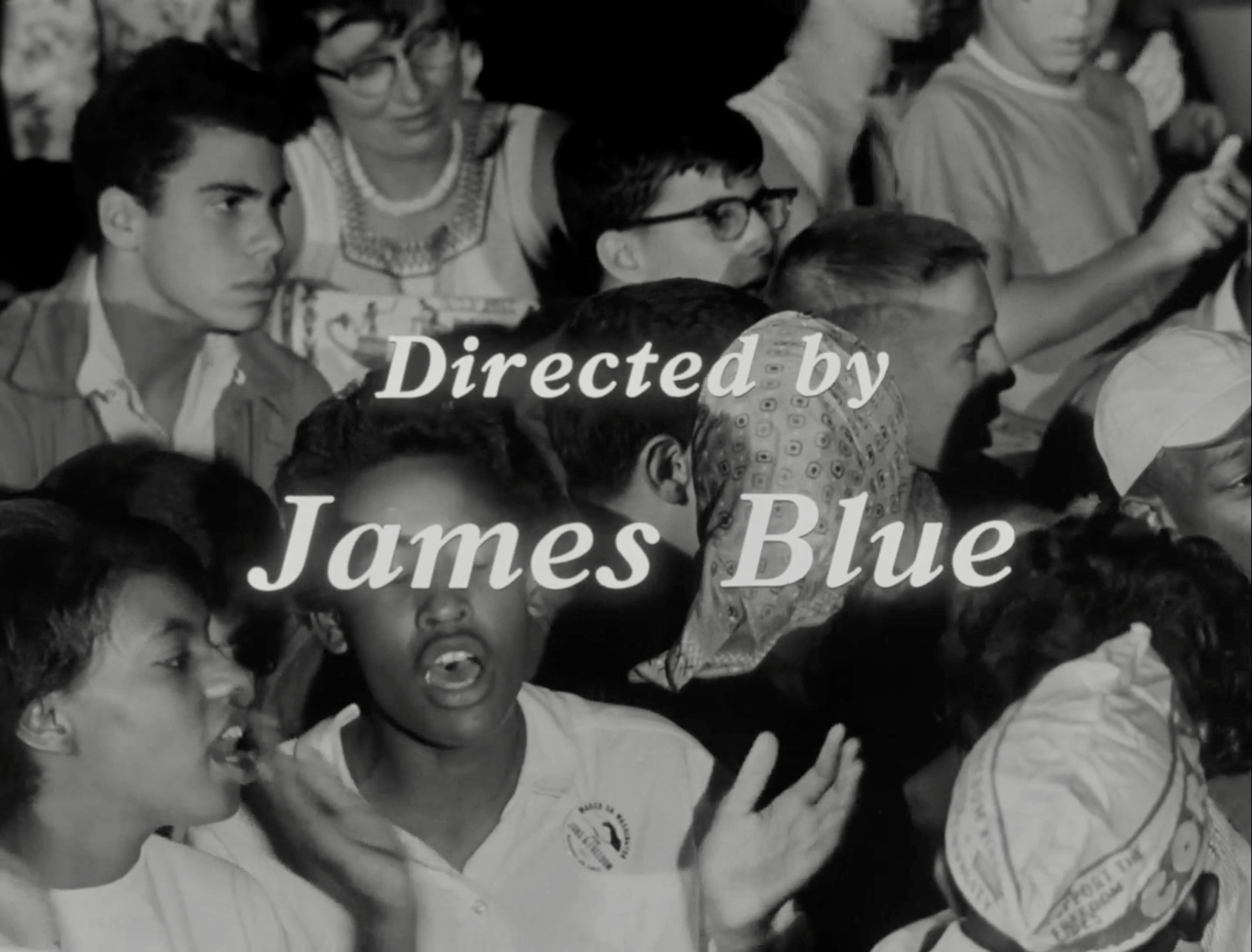 A film still showing people singing with the title "Directed by James Blue."
